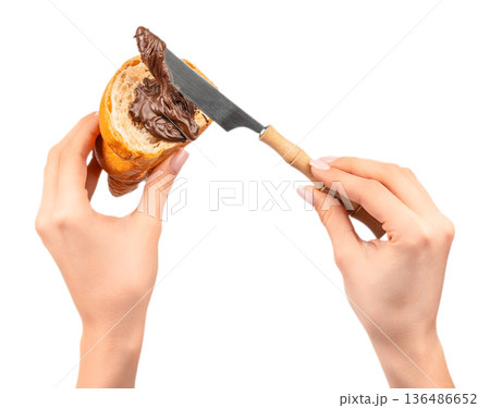 Spreading chocolate cream on croissant with knife in female hands isolated on white Spreading chocolate cream on croissant with knife in female hands isolated on white 136486652