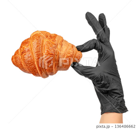Fresh croissant held by hand in black glove isolated on white background Fresh croissant held by hand in black glove isolated on white background 136486662