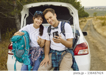 Travel adventure of happy couple sitting by car with smartphone to check map Travel adventure of happy couple sitting by car with smartphone to check map 136487424