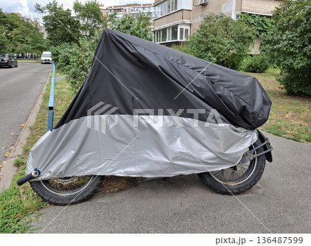 Black and gray cover on motorcycle parked in the yard of a buildings 136487599