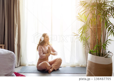 Adult caucasian woman meditating with headphones on yoga mat in hotel room Adult caucasian woman meditating with headphones on yoga mat in hotel room 136487705
