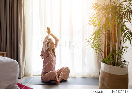 Adult woman practicing yoga pose on mat near window in hotel room 136487718
