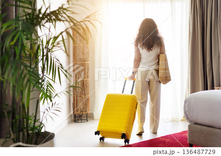 Rear view of woman standing near window with suitcase inside hotel room Rear view of woman standing near window with suitcase inside hotel room 136487729