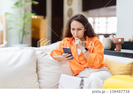 Thoughtful caucasian woman sitting on hotel sofa and checking smartphone Thoughtful caucasian woman sitting on hotel sofa and checking smartphone 136487738