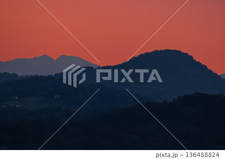 Mountain silhouettes at sunset with dramatic orange sky, serene landscape showcasing natural beauty. 136488824