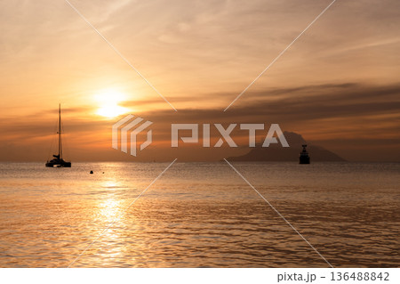 Ocean view with distant island and silhouettes of yachts Ocean view with distant island and silhouettes of yachts 136488842