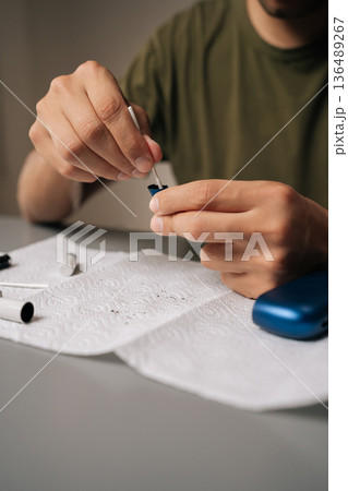 Close-up vertical cropped shot of man performing maintenance on electronic cigarette with cotton swab, ensuring optimal functioning and cleanliness for better vaping experience and improved hygiene. 136489267