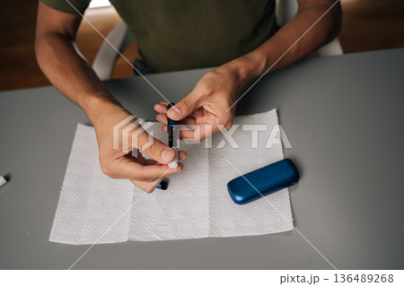 Close-up of unrecognizable man cleaning electronic cigarette emphasizing importance of hygiene and maintenance in vaping, sitting at table. Process of maintaining heated electronic cigarette device. Close-up of unrecognizable man cleaning electronic cigarette emphasizing importance of hygiene and maintenance in vaping, sitting at table. Process of maintaining heated electronic cigarette device. 136489268