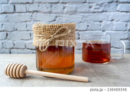Honey glass jar with honeycomb, cup of tee and wood spoon stay on the stone table. 136489348