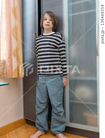 Vertical full body portrait of a barefoot boy standing by a wardrobe. Casual kid fashion Vertical full body portrait of a barefoot boy standing by a wardrobe. Casual kid fashion 136489359