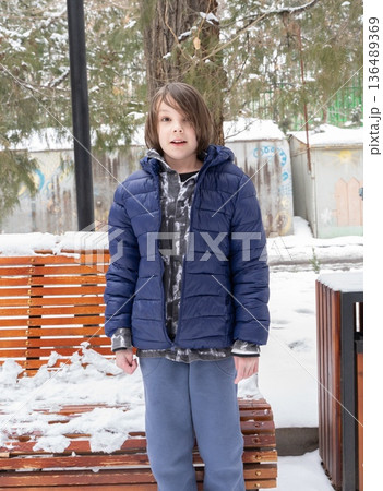 Young boy standing in snowy park. Child in blue winter jacket outdoors. Cold weather lifestyle Young boy standing in snowy park. Child in blue winter jacket outdoors. Cold weather lifestyle 136489369