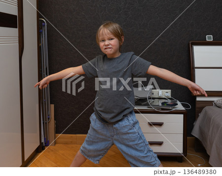Playful young boy making a funny grimacing face in a bedroom. Child with arms outstretched Playful young boy making a funny grimacing face in a bedroom. Child with arms outstretched 136489380