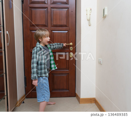 Surprised young boy reaching for door handle and shouting. Child yelling at home entrance side view 136489385
