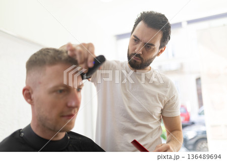 Professional barber cutting male client's hair in salon 136489694