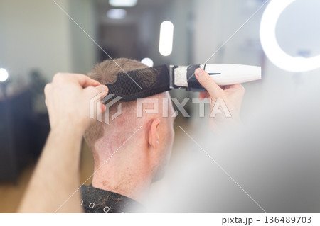 Hairdresser cutting client's hair with electric clipper Hairdresser cutting client's hair with electric clipper 136489703
