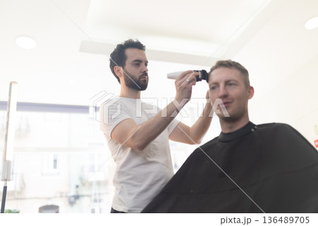 Barber giving haircut to young man using shaver Barber giving haircut to young man using shaver 136489705