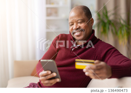 Middle aged black man using smartphone and holding credit card at home 136490473