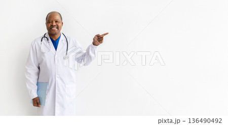 Mature black male doctor in white coat pointing aside while holding clipboard 136490492