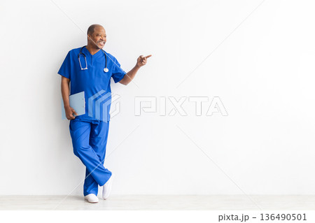 Mature black male doctor pointing aside at copy space while holding clipboard Mature black male doctor pointing aside at copy space while holding clipboard 136490501