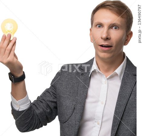 Surprised man holding a light bulb with an expression of excitement indoors 136490797