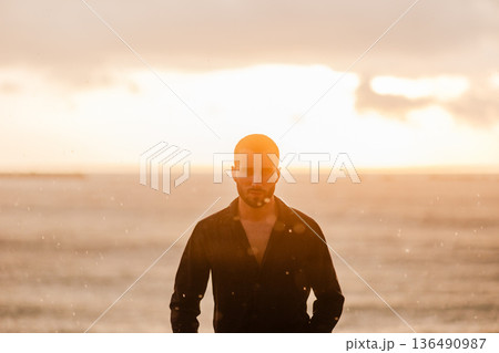 Young man standing by ocean at golden hour Young man standing by ocean at golden hour 136490987