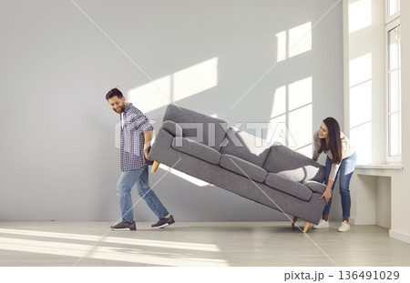 Happy young husband and wife move furniture and put new a sofa in the living room Happy young husband and wife move furniture and put new a sofa in the living room 136491029