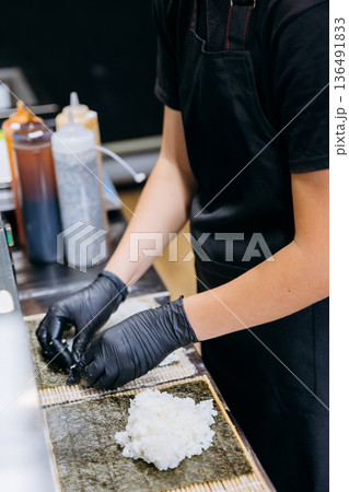 Chef in gloves spreads sushi rice on nori sheets for maki rolls in restaurant kitchen 136491833