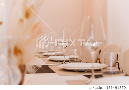 Wine glasses and place settings on elegant banquet table in soft neutral interior Wine glasses and place settings on elegant banquet table in soft neutral interior 136491870