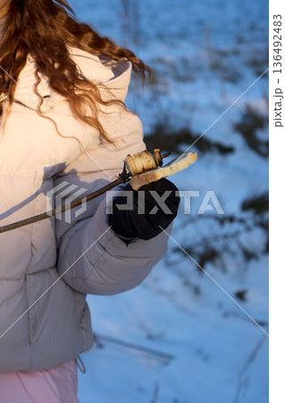 Enjoying winter: Person roasting onion and bread outdoors on a stick in snowy setting. Enjoying winter: Person roasting onion and bread outdoors on a stick in snowy setting. 136492483