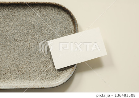 Closeup of minimal blank business card mockup on ceramic tray. Neutral beige background, top view stationery template. Modern branding presentation, elegant paper card with copy space, flatlay. Closeup of minimal blank business card mockup on ceramic tray. Neutral beige background, top view stationery template. Modern branding presentation, elegant paper card with copy space, flatlay. 136493309