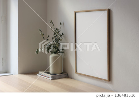 Minimal wooden picture frame mockup on beige wall near window. Olive branches in vase, table. Scandinavian interior, side view. Blank vertical poster template, neutral home. Natural light. Copy space Minimal wooden picture frame mockup on beige wall near window. Olive branches in vase, table. Scandinavian interior, side view. Blank vertical poster template, neutral home. Natural light. Copy space 136493310