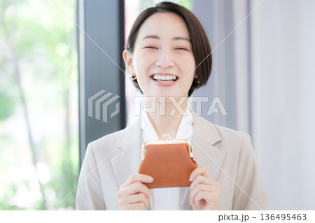 緑背景でお財布を持ってカメラ目線の笑顔のスーツを着た女性ビジネスシーン 緑背景でお財布を持ってカメラ目線の笑顔のスーツを着た女性ビジネスシーン 136495463