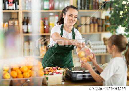 Woman sells fruits to girl, puts apples in bag, puts them on scale and weighs fruits Woman sells fruits to girl, puts apples in bag, puts them on scale and weighs fruits 136495925