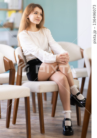 Portrait of pretty young female student dressed in white blouse and black skirt listening at lesson in university 136496073