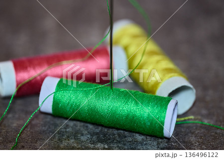 Macro shot of green, red, and yellow thread spools with a needle on a textured surface Macro shot of green, red, and yellow thread spools with a needle on a textured surface 136496122
