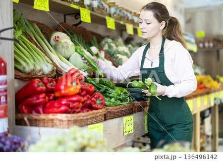 Saleswoman lays out green peppers on the counter 136496142