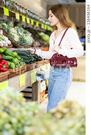 Girl selects ripe cucumers from counter in grocery store Girl selects ripe cucumers from counter in grocery store 136496164