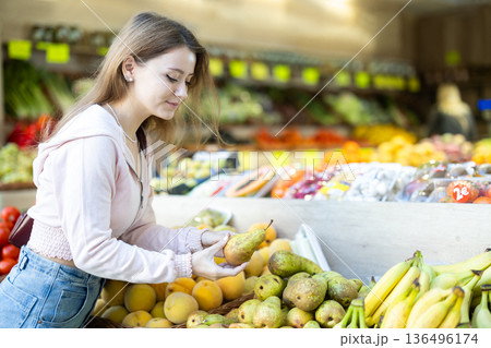 Young woman choosing a pear on the counter background 136496174