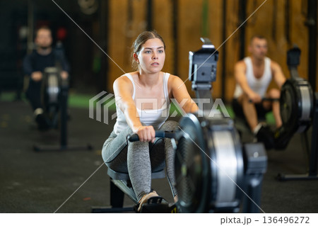 Determined young girl training with rowing machine in sports hall Determined young girl training with rowing machine in sports hall 136496272