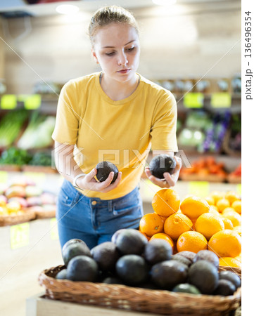 Teenage girl chooses avocado in store Teenage girl chooses avocado in store 136496354