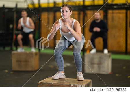 Sportive young girl squatting on box during crossfit workout Sportive young girl squatting on box during crossfit workout 136496381