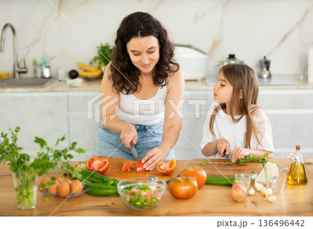 Mom and daughter dice up raw vegetables for salad on cutting boards. 136496442
