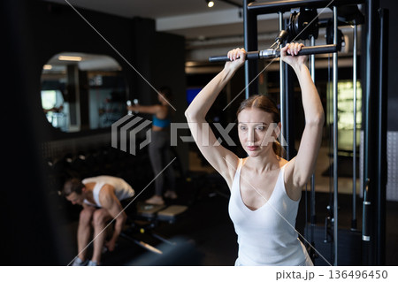 Sportive young girl training on cable exercise machine in gym Sportive young girl training on cable exercise machine in gym 136496450