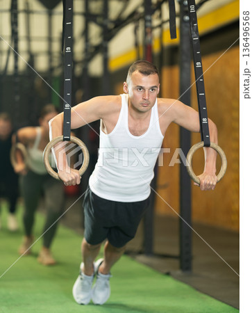 Sportive young guy working out with gymnastic rings in gym during crossfit workout Sportive young guy working out with gymnastic rings in gym during crossfit workout 136496568