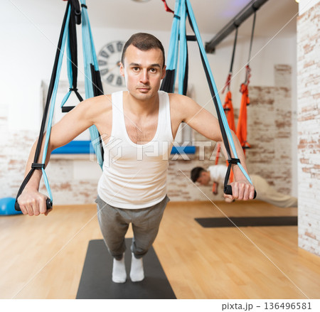 Man performing chest press with TRX straps during Pilates training 136496581