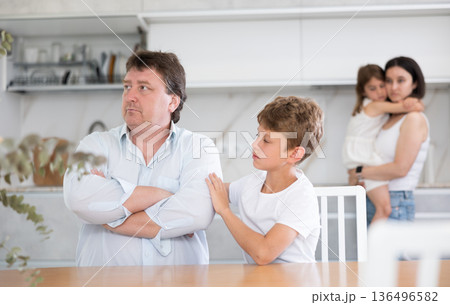 Frustrated man sits at kitchen table and tells wife and children about unforeseen difficulties 136496582