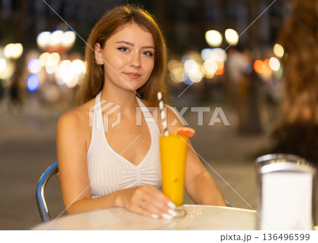 Woman sits at a table in a cafe overlooking the evening city of Barcelona 136496599