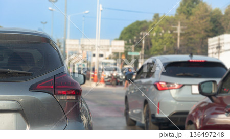 Rear side view of car driving on the road. Car is parked at the intersection. Background of city and trees under blue sky. Rear side view of car driving on the road. Car is parked at the intersection. Background of city and trees under blue sky. 136497248