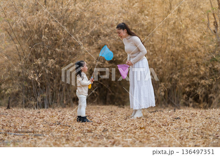 Mother and child girl bonding while playing with butterfly nets in dry forest. 136497351