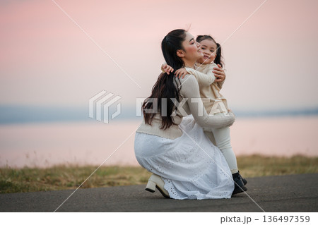 Heartwarming moment of mother and daughter hugging by lakeside at sunset Heartwarming moment of mother and daughter hugging by lakeside at sunset 136497359